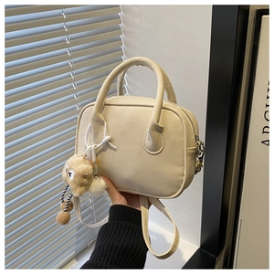 Close-up of cream textured baguette bag with a cute plush puppy charm and round handle