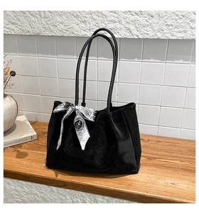 Detail of a black suede tote bag with a vintage printed silk scarf on a wooden surface