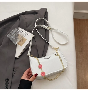 Detail of white lychee leather handbag with a stylish strawberry charm and gold metal chain