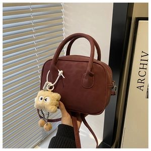 Detail of wine red matte leather crossbody bag with a playful brown plush charm