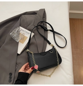 Detail of black pebbled leather handbag with gold chain and strawberry charms