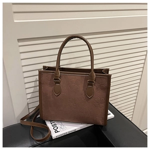 Détail du sac cabas en daim marron avec trèfle gaufré et poignées cylindriques robustes