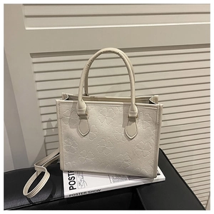 Détail du sac cabas crème avec gaufrage trèfle et poignées rondes sur siège en cuir