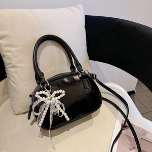 Elegante borsa baguette nera lucida con fiocco di perle e pizzo su una sedia minimal