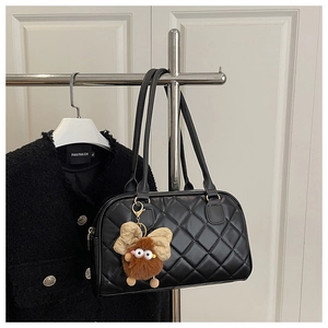 Detail of black quilted tote bag with gold hardware and a cute brown monster pendant