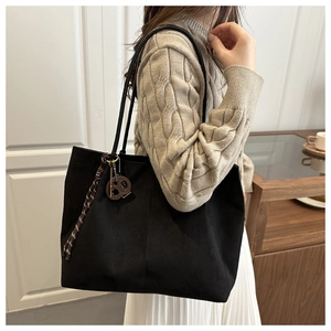 Close-up of black suede tote bag featuring a circular letter charm and woven tassel detail
