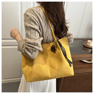Detail of a large ginger yellow suede tote bag with a decorative checked ribbon charm