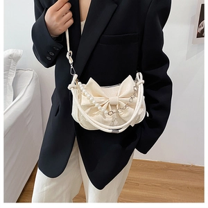 Detail of creamy white crossbody bag featuring a large bow and pearl chain decoration