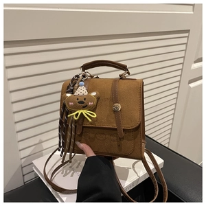Detail of warm brown suede crossbody bag with gold round clasp and bear charm accessory