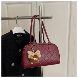 Detail of burgundy quilted shoulder bag with chic plush charm and stitching pattern