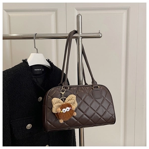 Close-up of brown quilted bowling bag with double handles and a plush monster charm