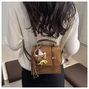 Detail of vintage brown suede backpack with teddy bear charm and metallic buckle
