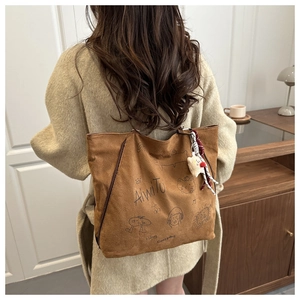 Sac cabas en daim marron avec graffiti porté par un mannequin dans un décor clair
