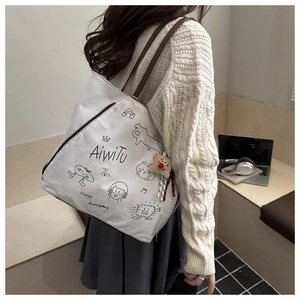 Détail du sac cabas en toile blanche avec anses marron et motifs de personnages dessinés à la main