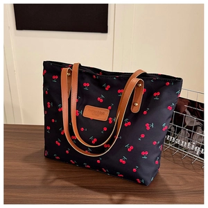 Détail d'un cabas en toile noire avec imprimé cerises et bretelles en cuir marron