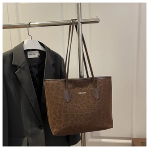 Detail of leopard print tote bag with white FASHION text and brown leather handles