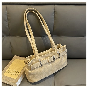 Détail du sac bandoulière beige en daim avec boucle argentée sur canapé en cuir