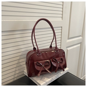 Detail of burgundy patent leather bag featuring bow accents and glossy mirror finish