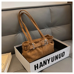 Détail du sac bandoulière en daim marron avec boucle argentée dans sa boîte de présentation