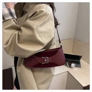 Detail of burgundy large shoulder bag with silver buckle worn with a beige trench coat
