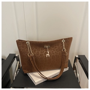 Detail of leopard print tote bag with gold chain strap and deer charm on leather chair