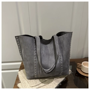 Détail d'un sac cabas gris vintage avec rivets argentés sur une table en bois avec café