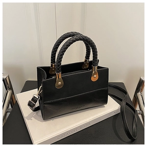 Detail of black leather handbag featuring woven handles and gold hardware accents