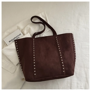 Détail d'un sac cabas en daim marron foncé avec des rivets argentés sur fond blanc texturé