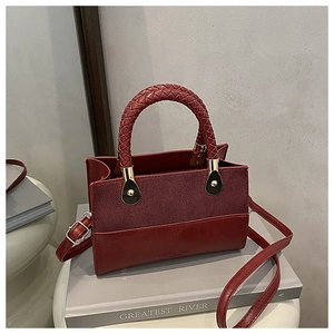Burgundy contrast handbag with woven handle and gold hardware on grey books