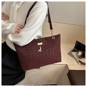 Detail of burgundy leopard print tote bag with gold chain strap and deer charm accent