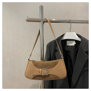 Detail of tan brown patchwork baguette bag with metal buckle hanging on a hanger