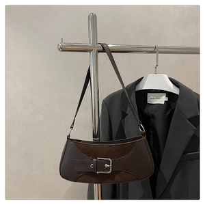 Detail of a brown leather shoulder bag with silver buckle strap against a grey wall