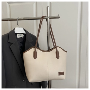 Close-up of cream leather tote bag featuring contrast brown handles and logo patch