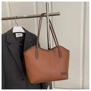 Detail of large brown tote bag with pebble leather texture and fashion label hanging on rack