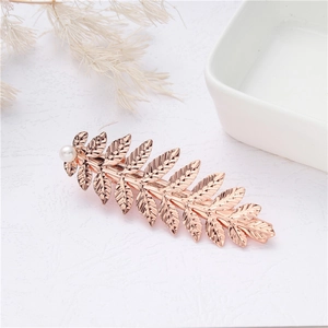 Macro view of rose gold leaf-shaped hair clip with pearls and intricate metal textures