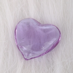 Translucent purple heart-shaped glass oil bottle on a soft white plush background