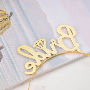 Detailed view of golden metal bride headband with artistic lettering and ring icon