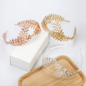 Elegant gold, silver, and rose gold leaf tiara headbands displayed on a wooden tray