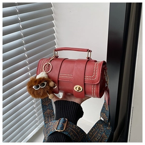 Detail of red cylindrical handbag with gold rivets, retro wide strap and plush pendant