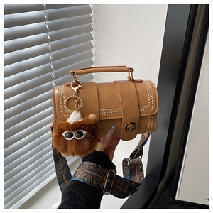 Detail of vintage brown cylinder crossbody bag with wide geometric strap and plush charm