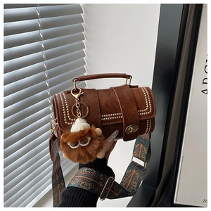 Detail of vintage brown cylinder bag featuring gold studs and lion plush charm accessory