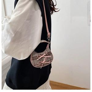 Detail of checkered shoulder bag with pink bows and leather strap on model