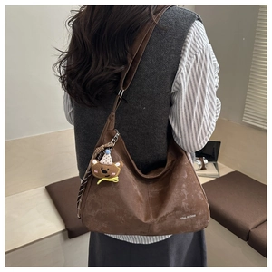 Detail showing the dark brown hobo bag with teddy bear charm and logo text