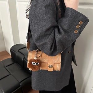 Vintage tan leather crossbody bag with stitching and fuzzy monster charm on a model