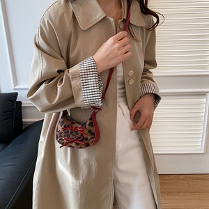 Leopard print crescent crossbody bag with red bows worn over a classic khaki trench coat