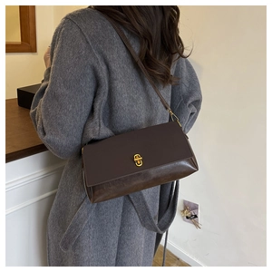 Detail of a dark brown leather crossbody bag with gold buckle on a grey wool coat