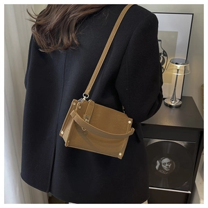 Brown leather crossbody bag with gold hardware shown on model with black blazer