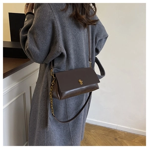 Detail of dark brown leather crossbody bag with gold twist lock and chain strap on coat