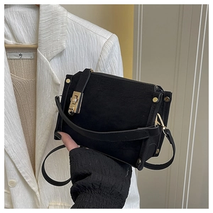 Detail of black suede square bag with gold twist lock, rivets, and shoulder strap