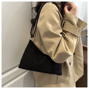 Detail of black knit shoulder bag with geometric texture and leather strap on a trench coat